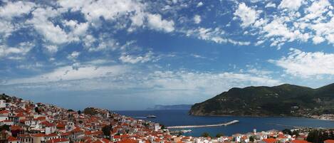 A coastal town with white buildings and red roofs, a harbor, and a mountainous backdrop.