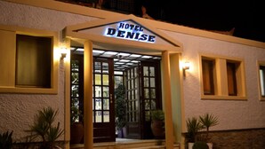 Hotel Denise with a sign above the entrance, a set of stairs leading up to the doors, and potted plants on either side.