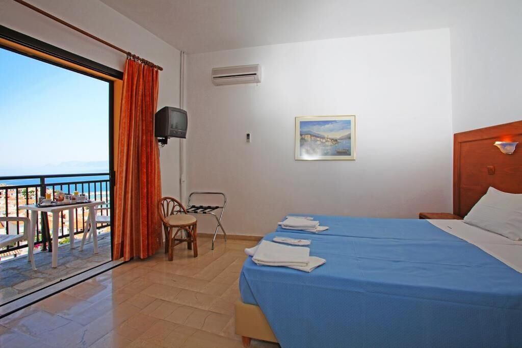 A hotel room with a balcony, a bed with blue bedding, a chair, a television, and a painting on the wall.