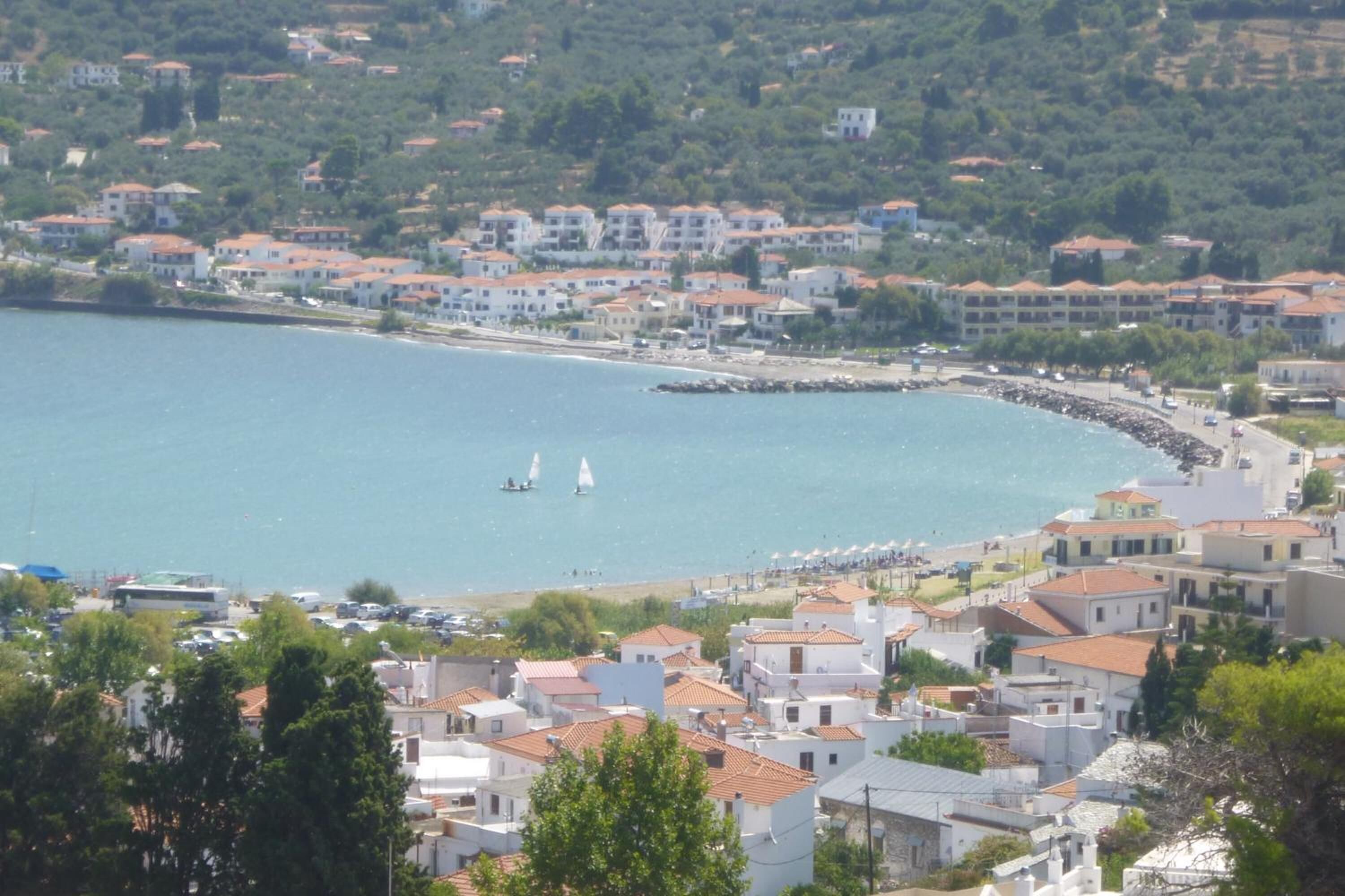 A coastal town with buildings along the waterfront, a beach, and sailboats in the water.