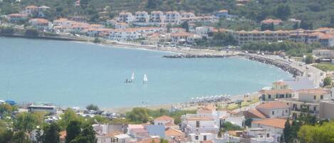 A coastal town with buildings along the waterfront, a beach, and sailboats in the water.