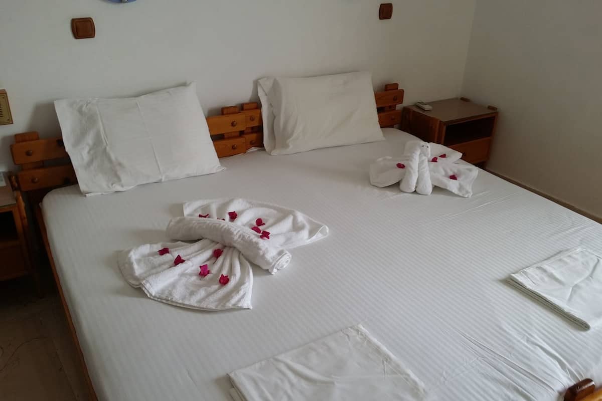 A neatly made bed with white linens, a wooden headboard, and a wooden nightstand with a lamp.