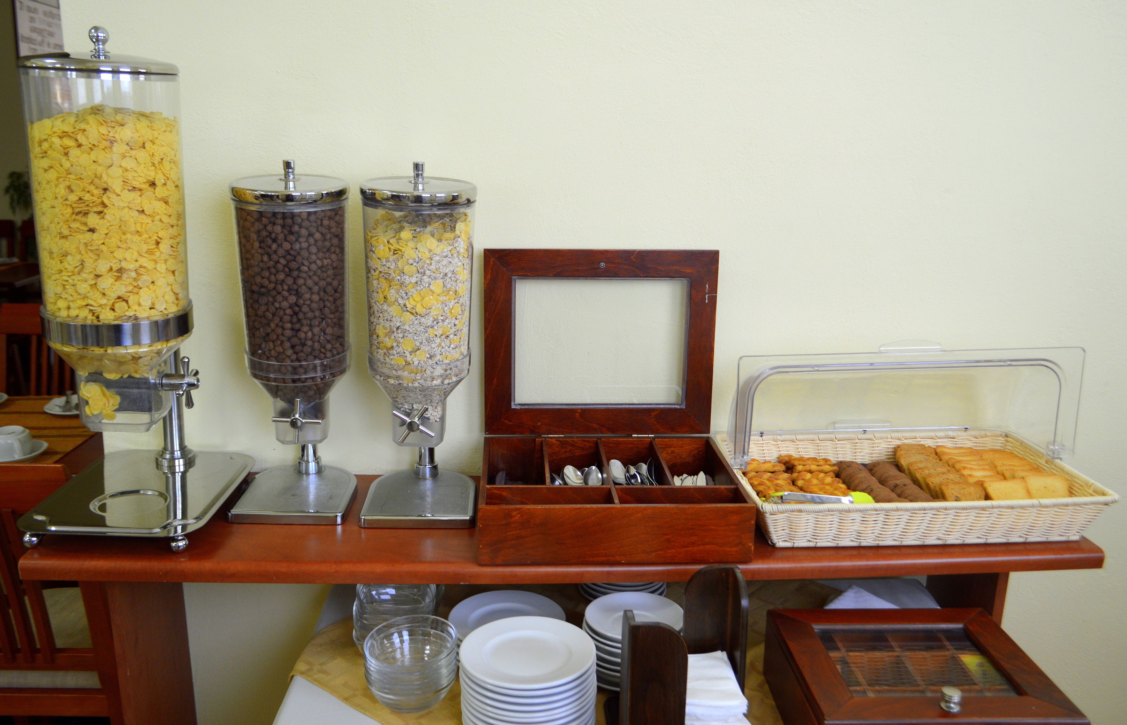 Montaje de un bufé de desayuno con dispensadores de cereales, cestas de pan y un dispensador de servilletas.