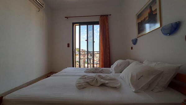 A hotel room with a bed, a view of the city through a window, and a painting on the wall.