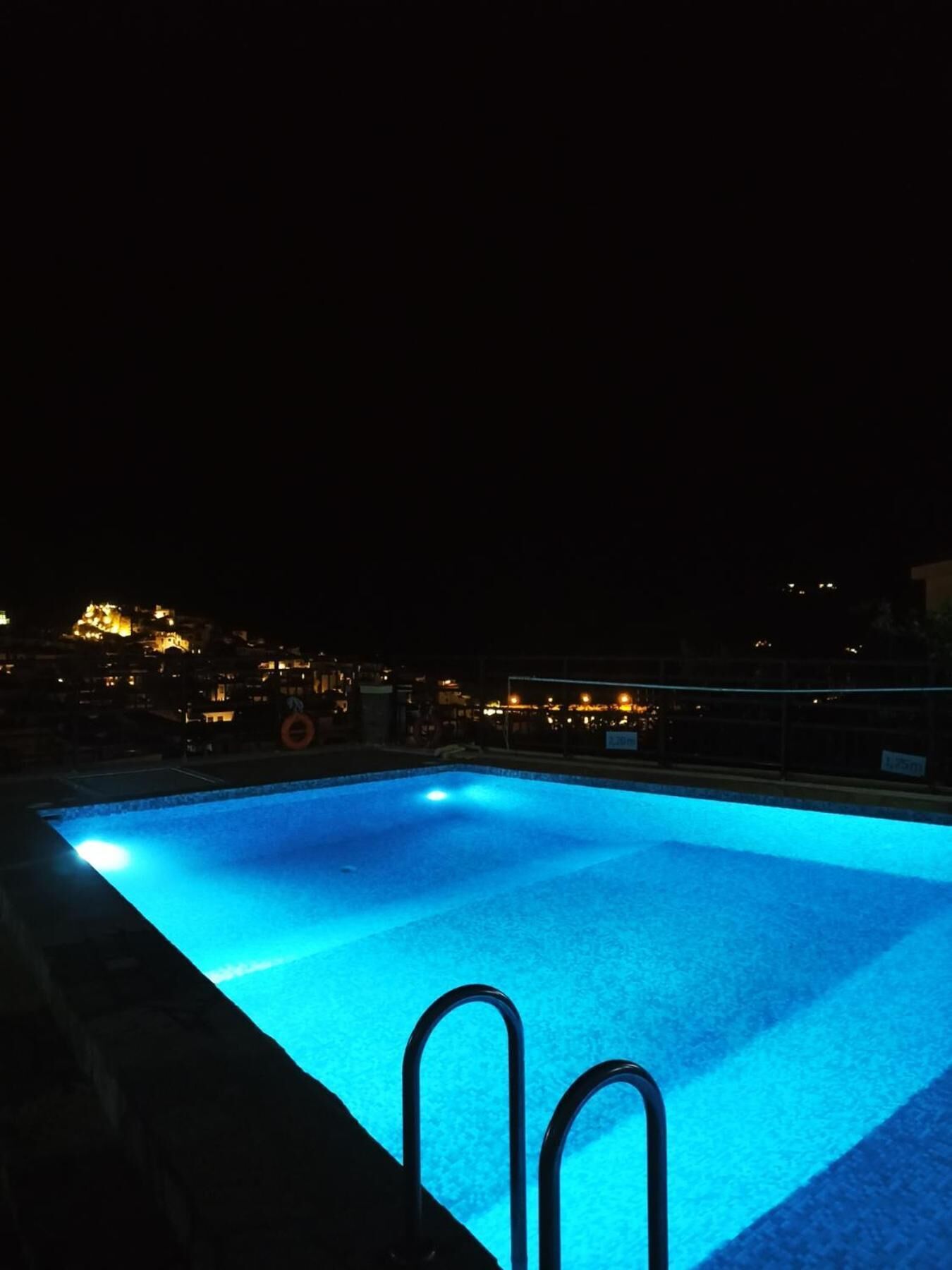 A swimming pool at night with a view of city lights in the background.