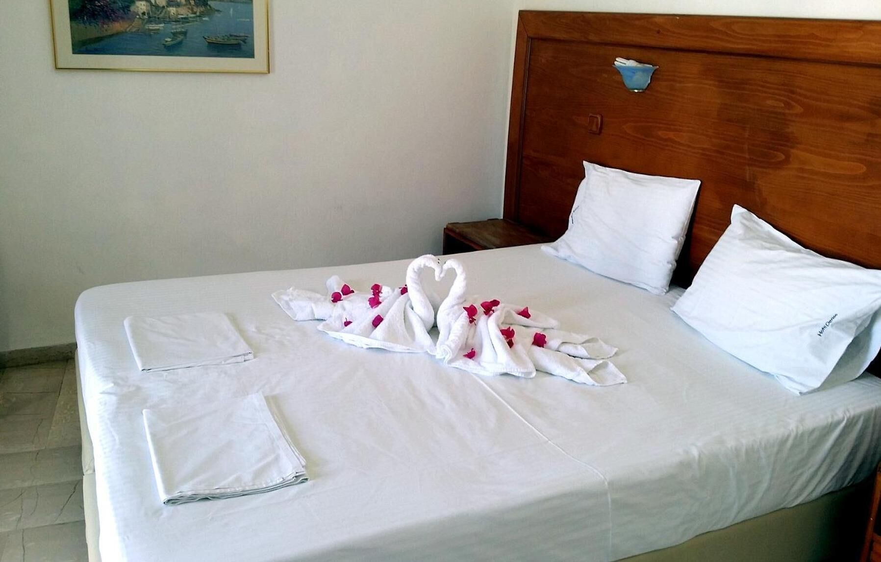 A hotel room with a neatly made bed, white linens, and a decorative swan towel arrangement.
