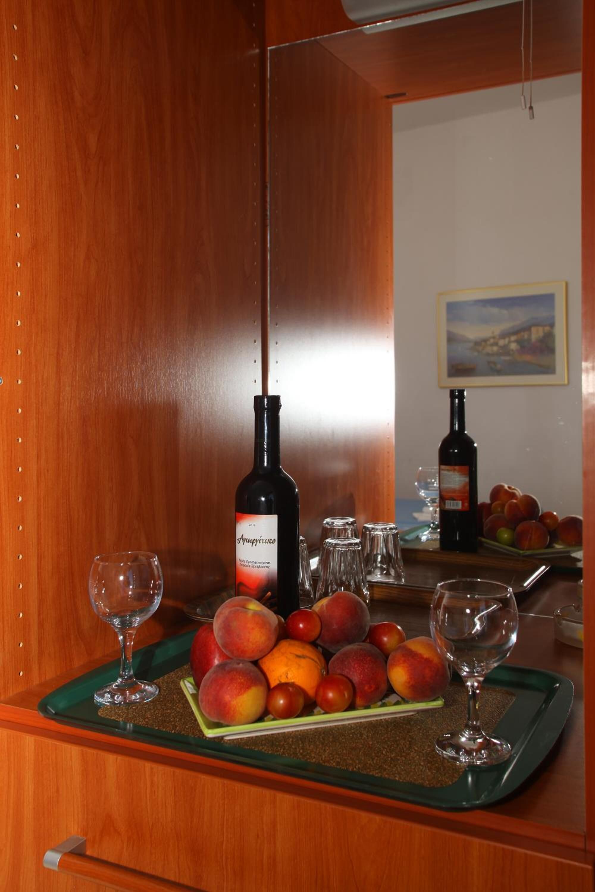 A wooden cabinet with a wine bottle, glasses, and a tray of fruit.