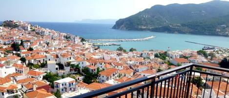 A coastal town with white buildings and red roofs, a pier, and a mountainous backdrop.