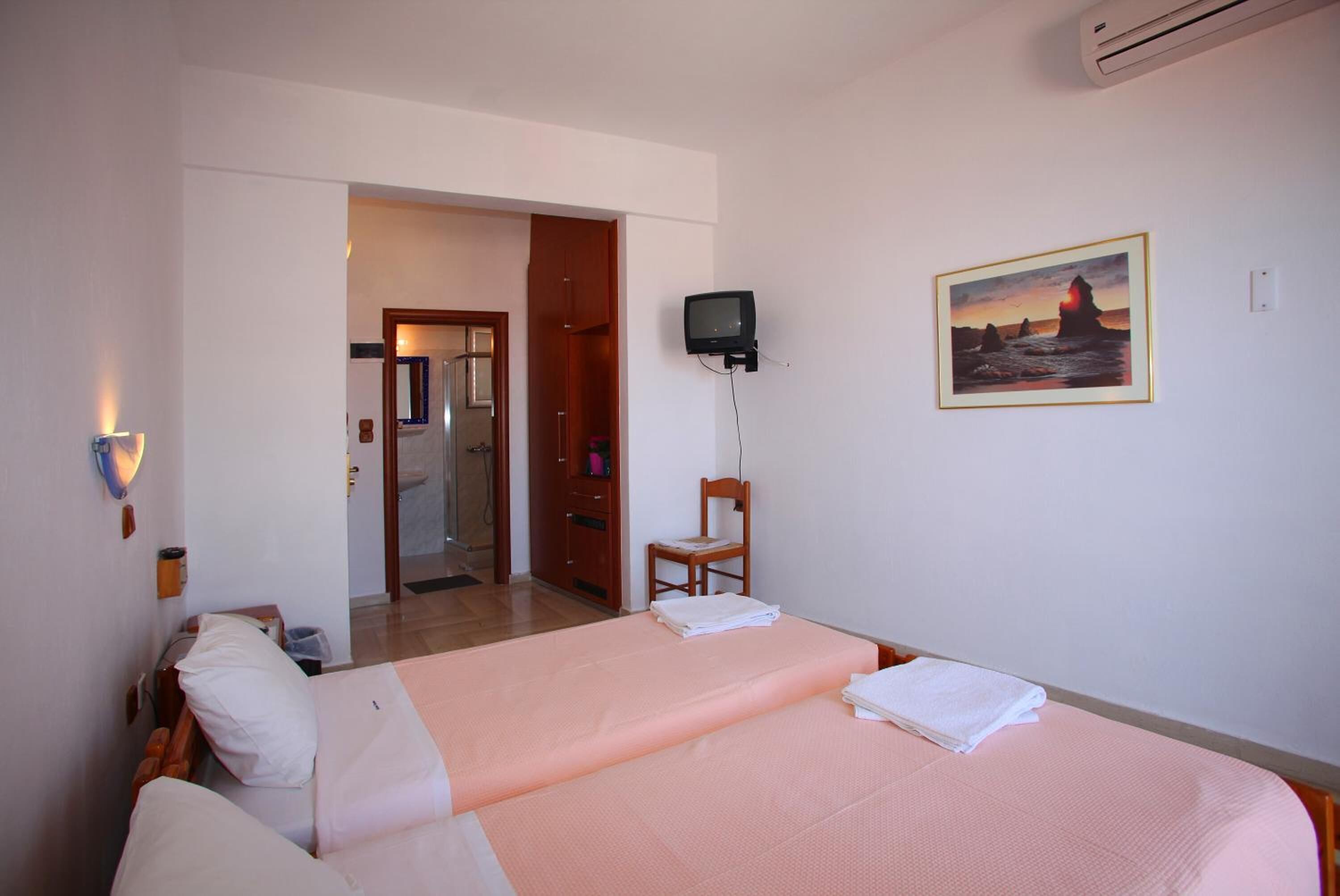 A hotel room with two beds, a television, a painting, and a bathroom visible through an open door.