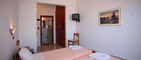 A hotel room with two beds, a television, a painting, and a bathroom visible through an open door.