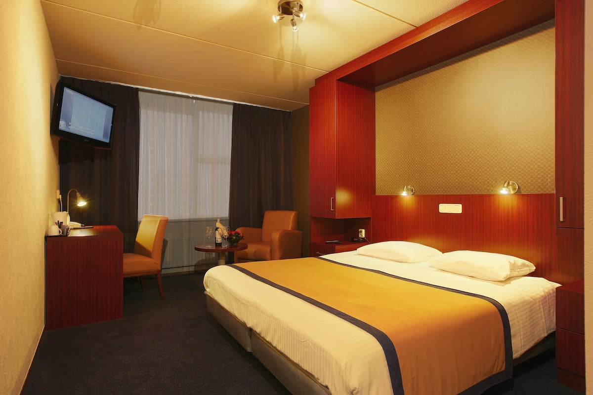 Habitación de hotel con una cama grande, un escritorio con computadora, una silla y televisión en la pared.