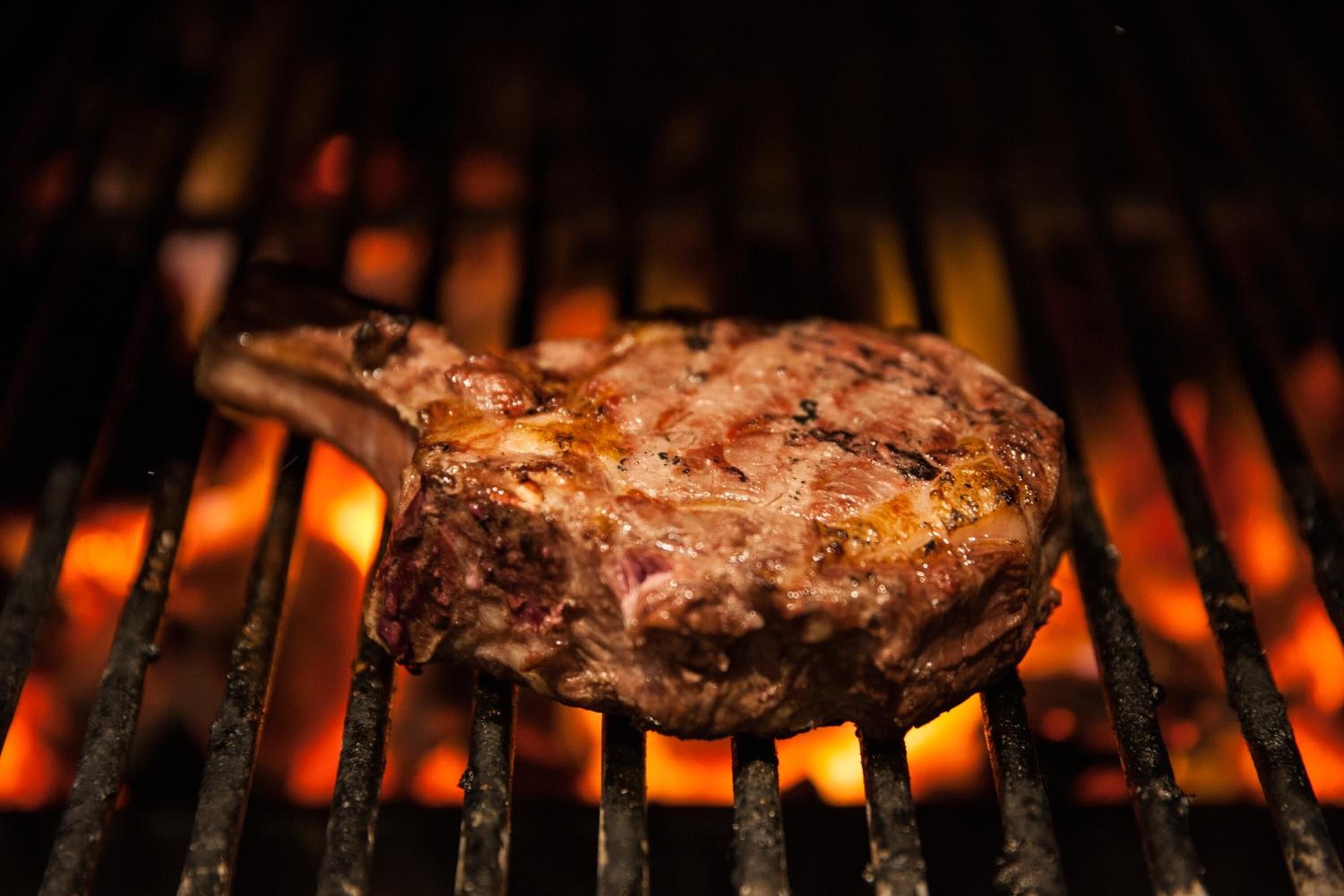 A steak grilling on a grill with visible flames.