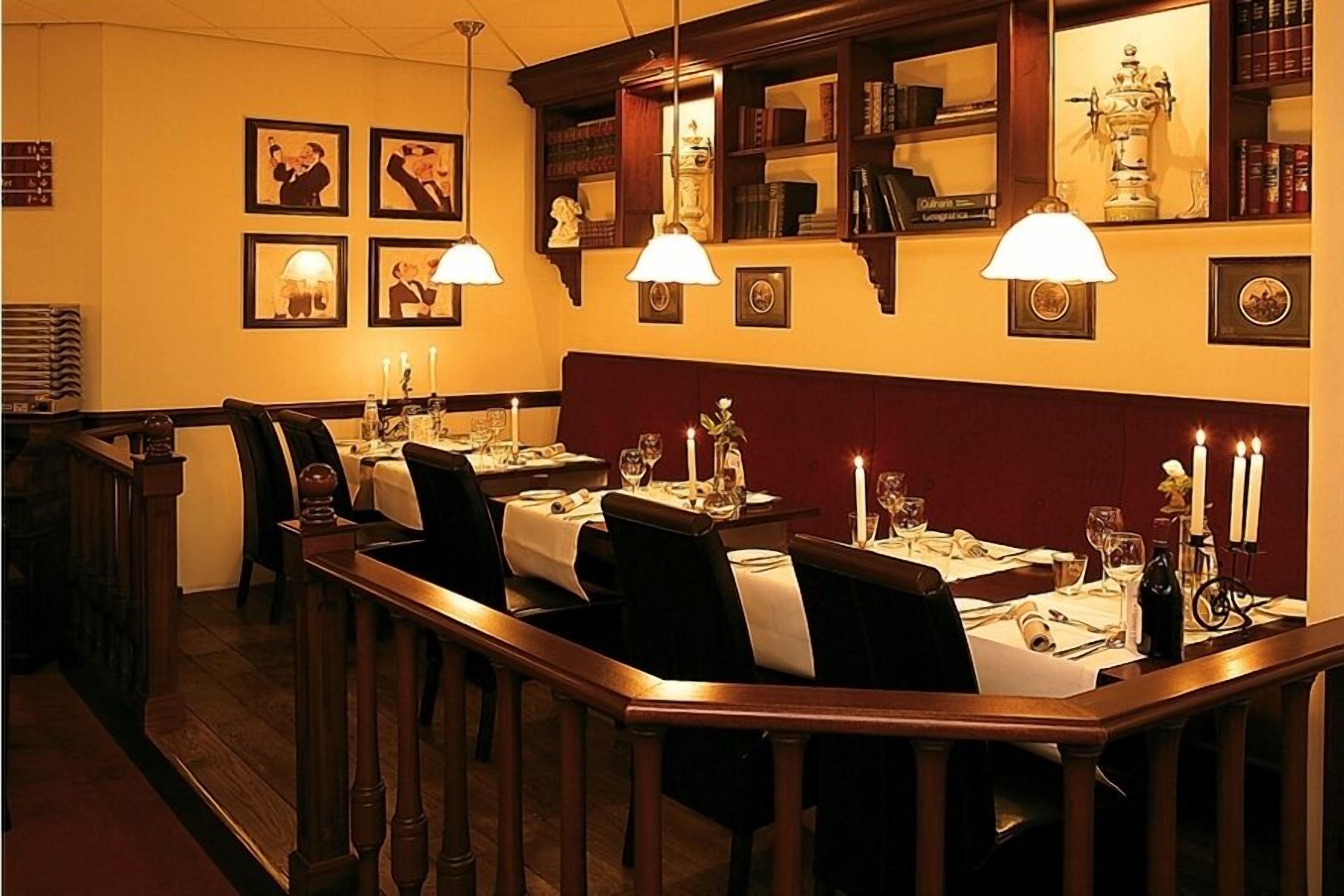 Un restaurant poc il·luminat amb mobles de fusta, taules amb espelmes i quadres als murs.