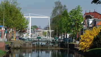 A canal with a white bridge structure, surrounded by greenery and buildings.