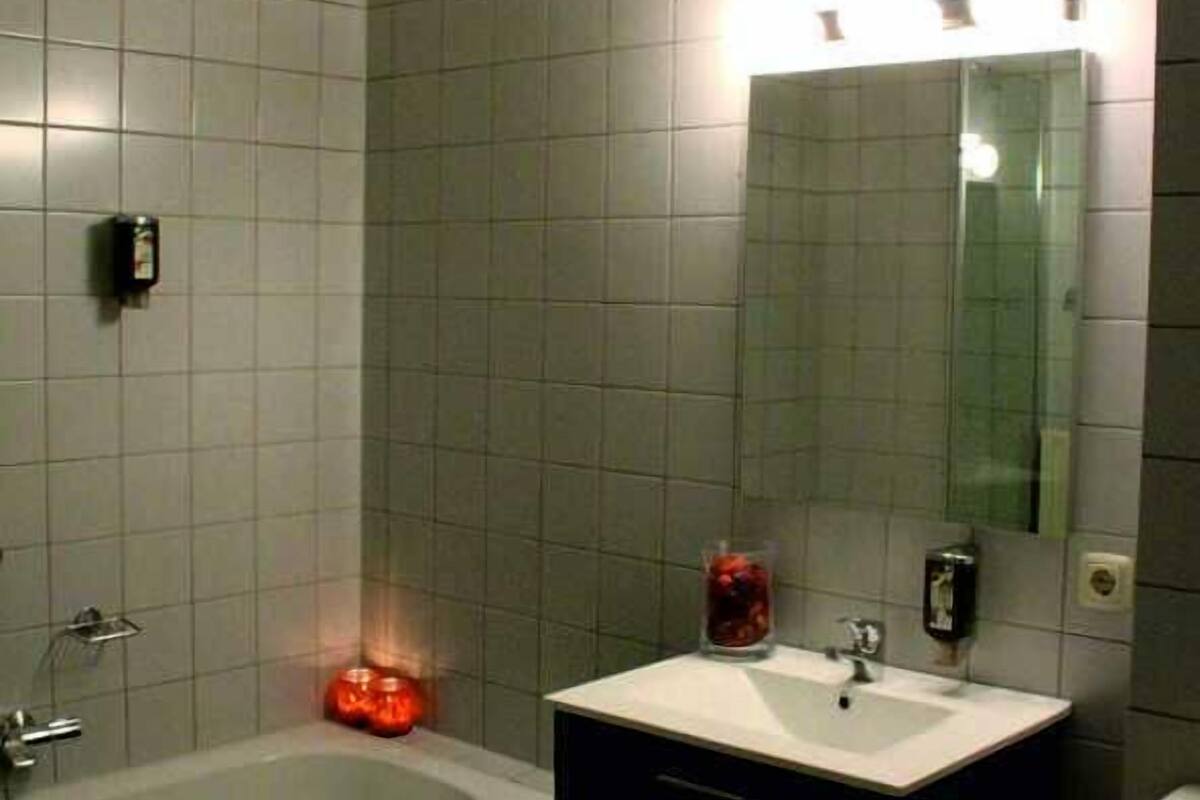 Un baño con bañera, lavabo con espejo y dispensador de jabón.