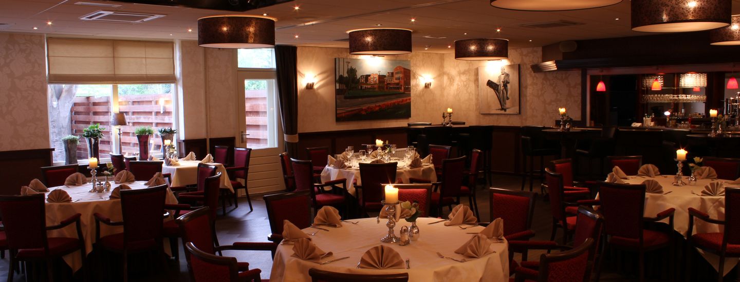 A restaurant with multiple tables set for dining, featuring candle centerpieces and red chairs.