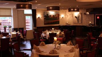 A restaurant with multiple tables set for dining, featuring candle centerpieces and red chairs.