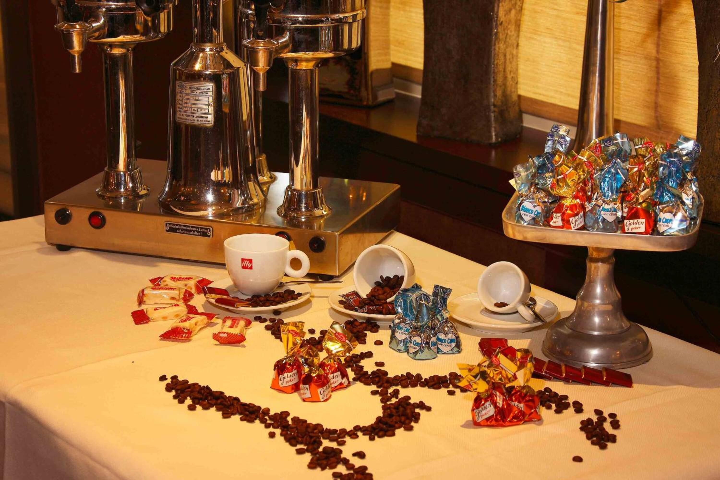 A table with a coffee machine, cups, and various chocolate and coffee packets.