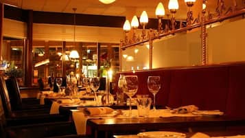 A restaurant interior with tables set for dining, overhead lighting fixtures, and a view of the street outside.