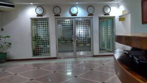 Un hall d’entrée avec un sol carrelé, un comptoir de réception et trois portes en verre, chacune surmontée d’une horloge.