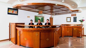 Un comptoir d’accueil où sont assis trois employés, un tableau encadré accroché au mur et un panneau indiquant que les locaux se trouvent au 5e étage.