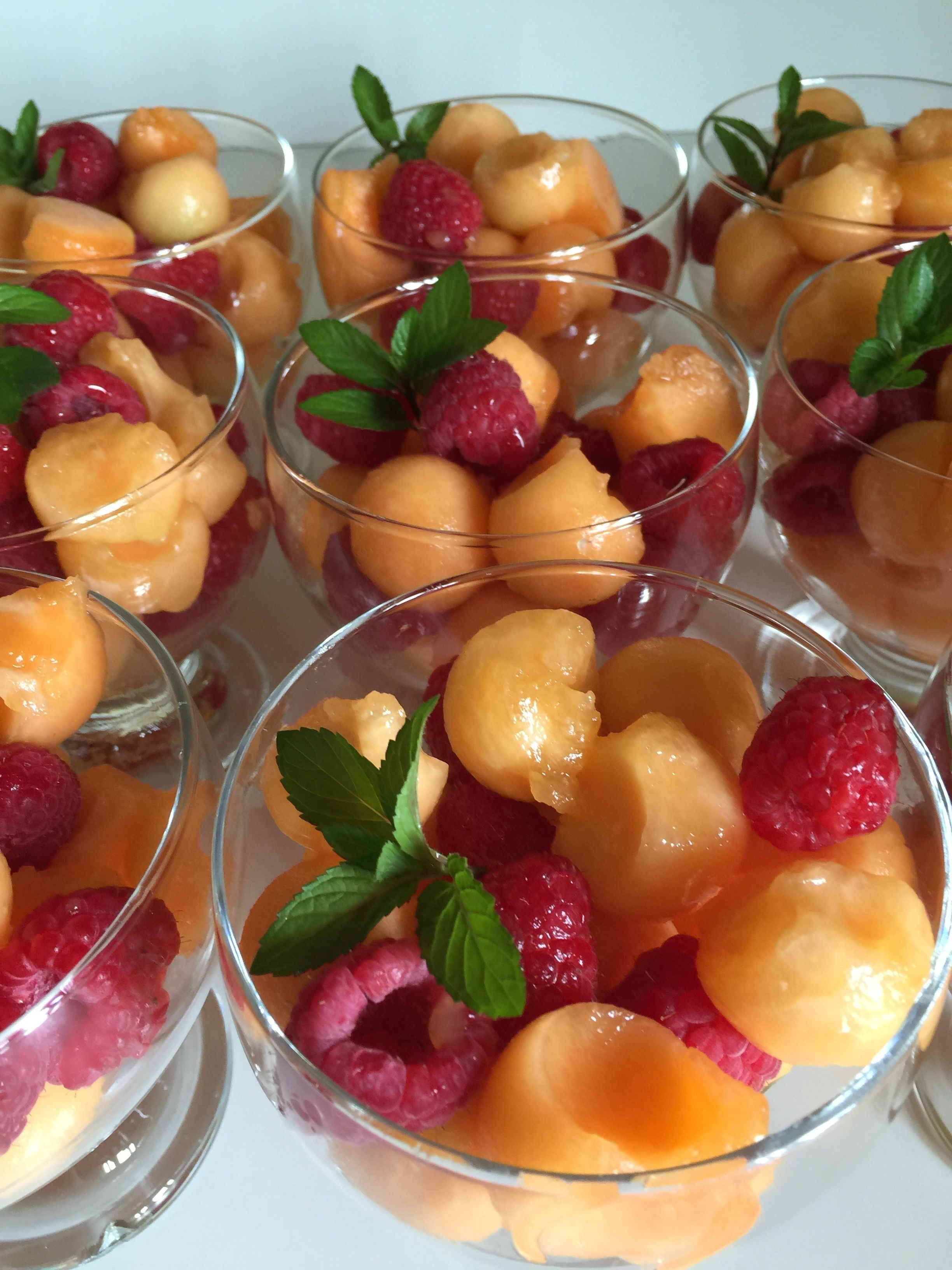 Mehrere transparente Gläser mit gewürfelter Cantaloupe-Melone und Himbeeren, garniert mit Minzblättern.
