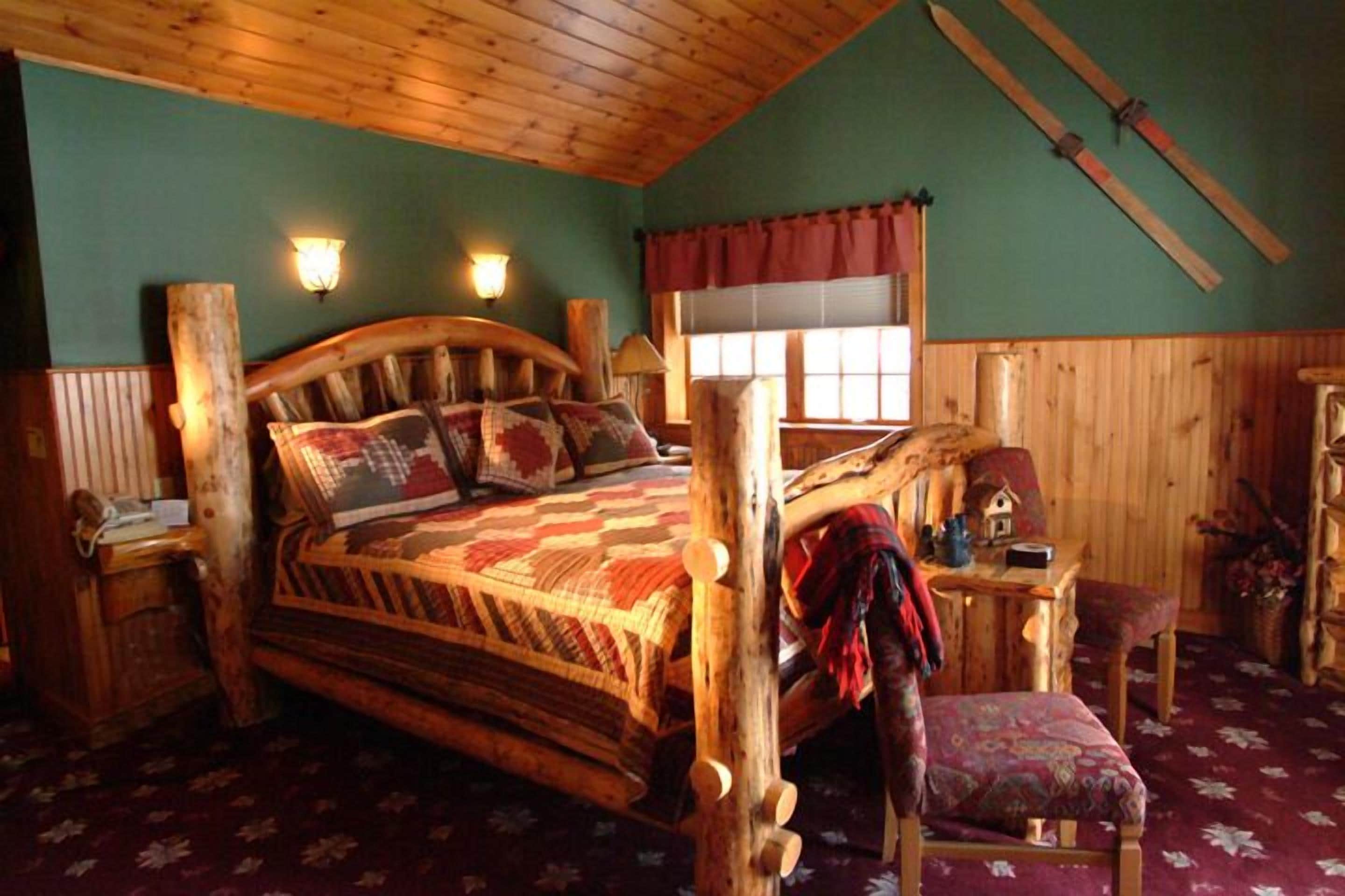 Ein rustikales Schlafzimmer aus Holz mit einem großen Bett, zwei Nachttischen, einem Fenster mit Vorhängen und einer Holzbalkendecke.