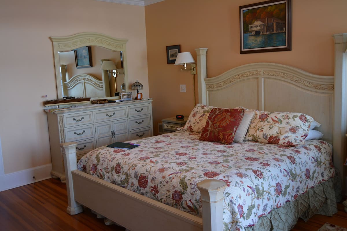 A bedroom with a bed, dresser, nightstand, lamp, and a painting on the wall.