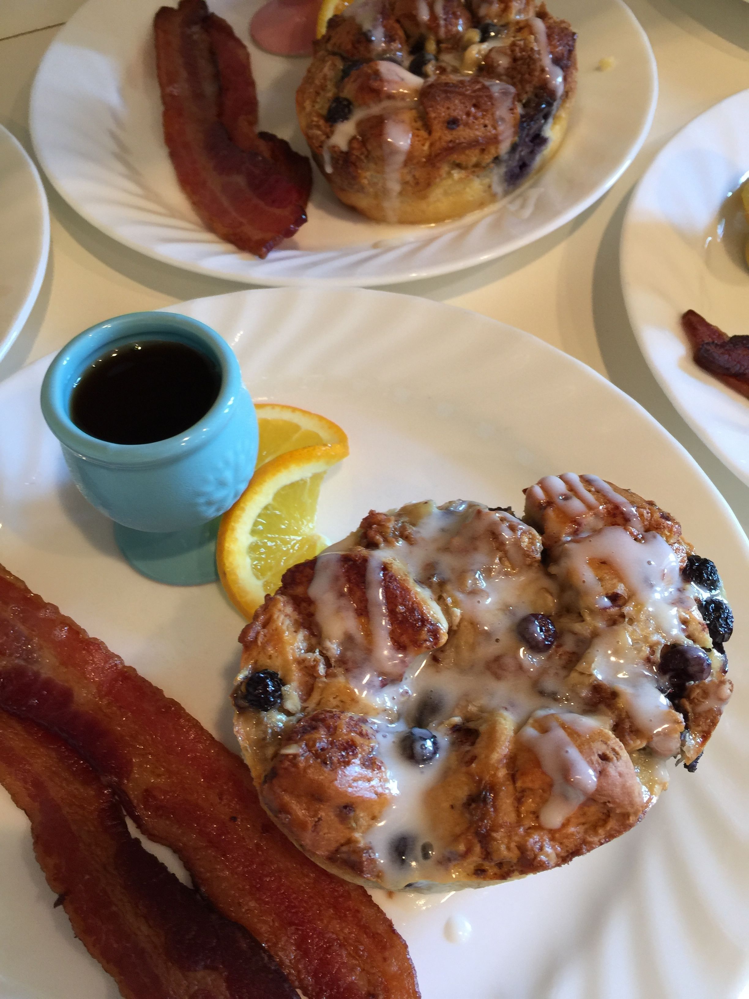 Un plato de desayuno con un muffin de arándanos, tocino y una taza de café.