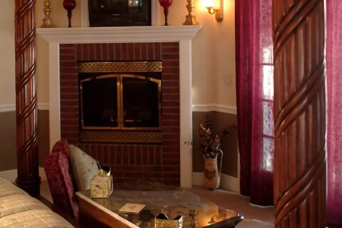 A room with a fireplace, a ceiling fan, and a bed with a headboard.