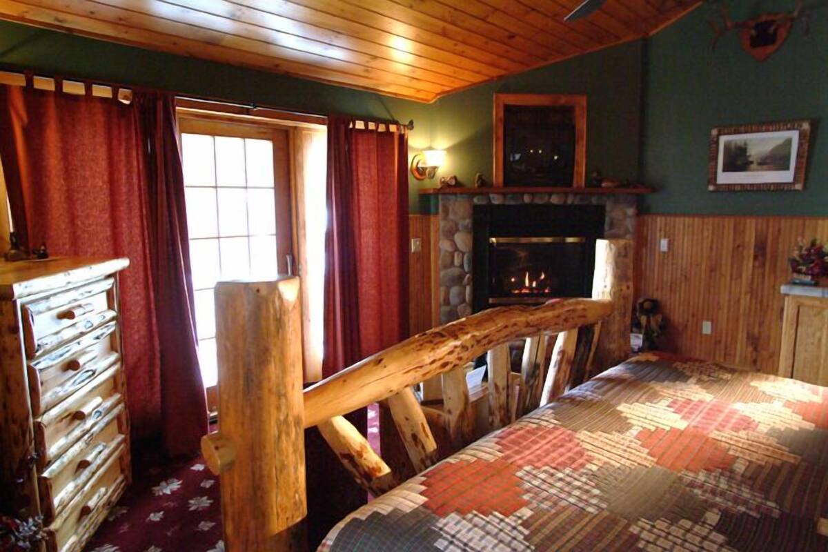 A cozy room with a wooden bed, a fireplace, and a stone wall.