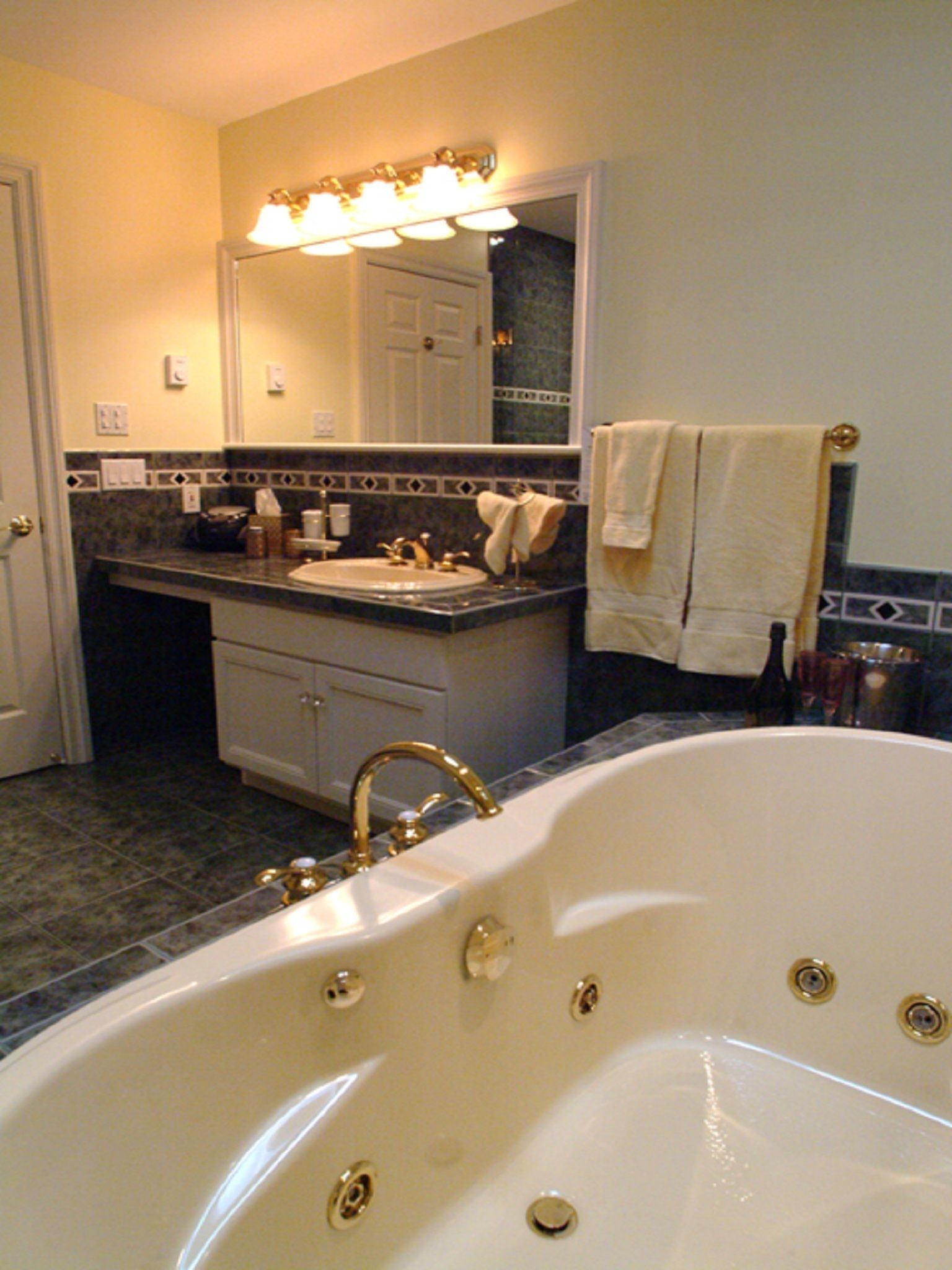 A bathroom with a large bathtub, a sink with a vanity, a mirror with lights, and a towel rack.