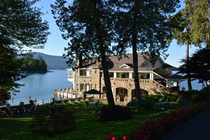A lakeside property with a stone building, outdoor seating, and a dock. - Boathouse Waterfront Lodging (Bolton Landing)