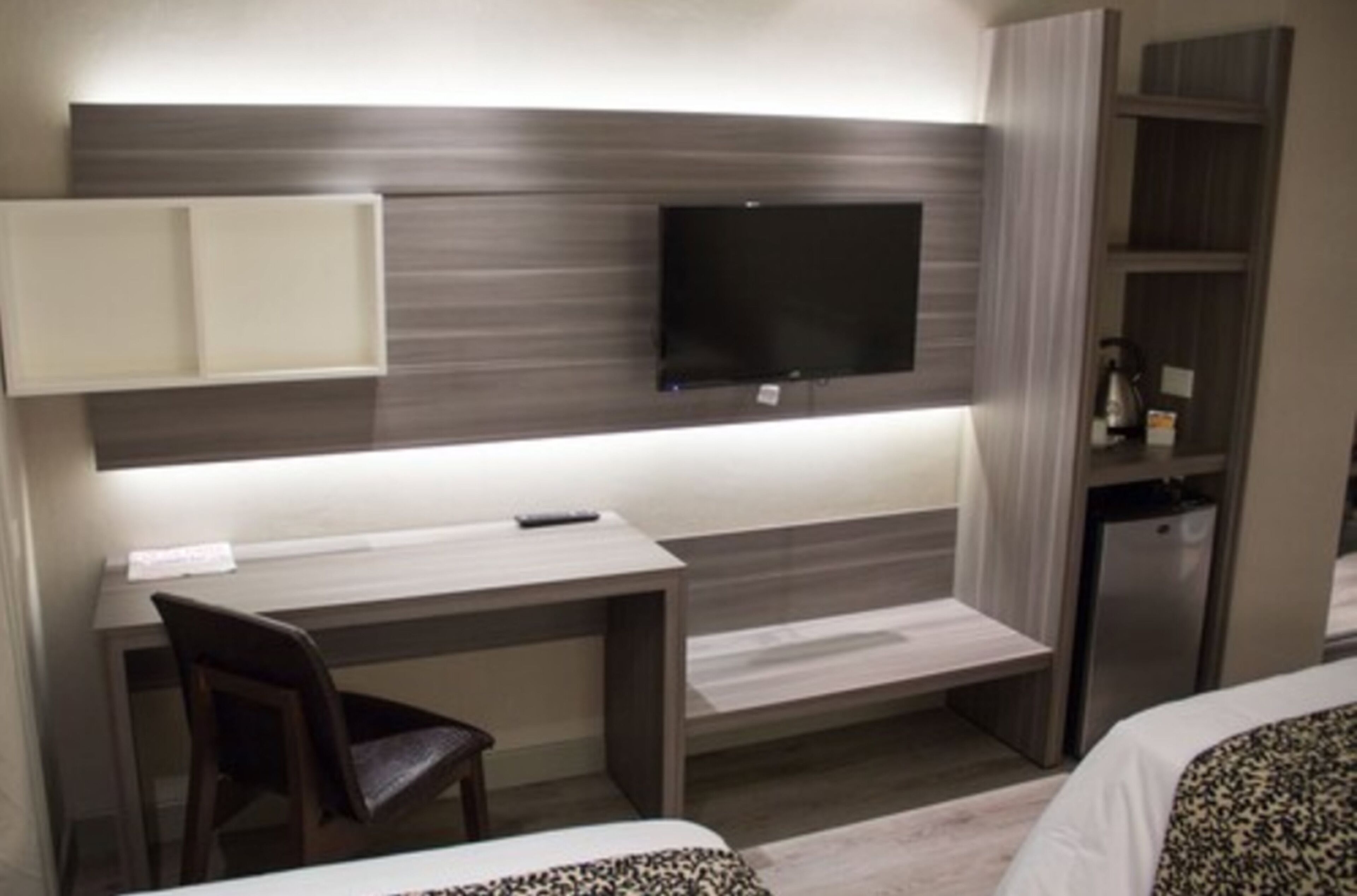 A hotel room with a desk, chair, TV, and a minibar.