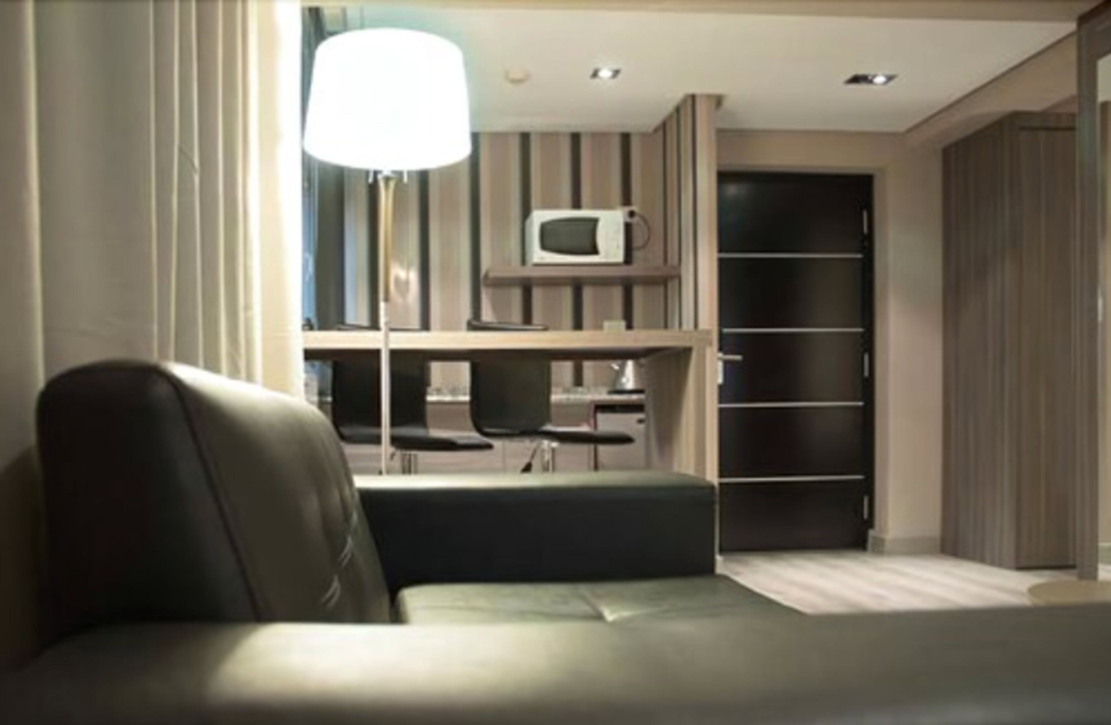 A modern room with a sofa, a desk with a chair, a microwave, and a wardrobe.