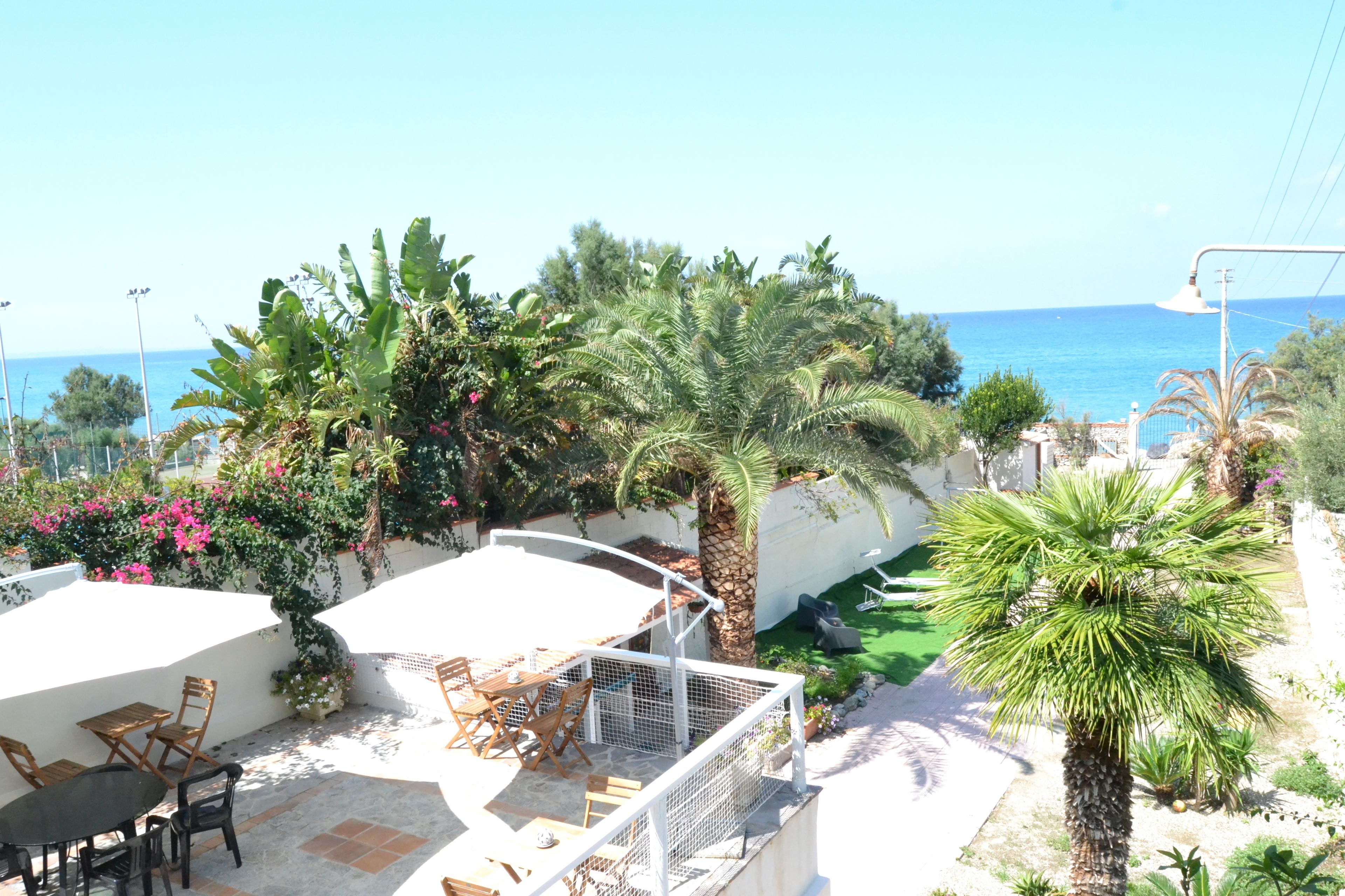 A patio area with outdoor furniture, a white wall, and a view of the sea.