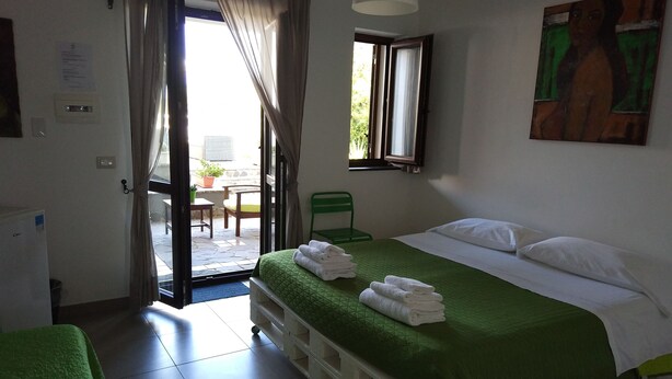 A hotel room with a bed, a green sofa, a window with curtains, a painting on the wall, and a view of the outside. - La Casa a Mare (Messina)