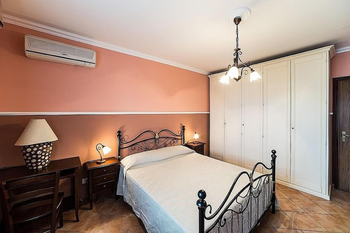 A bedroom with a bed, bedside tables, a desk, a lamp, and a wardrobe.