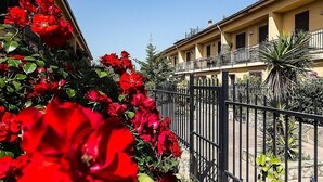 A building with a balcony, surrounded by a black metal fence, and red flowers in the foreground. - Bed & Breakfast Marina D'Aspra (Bagheria)