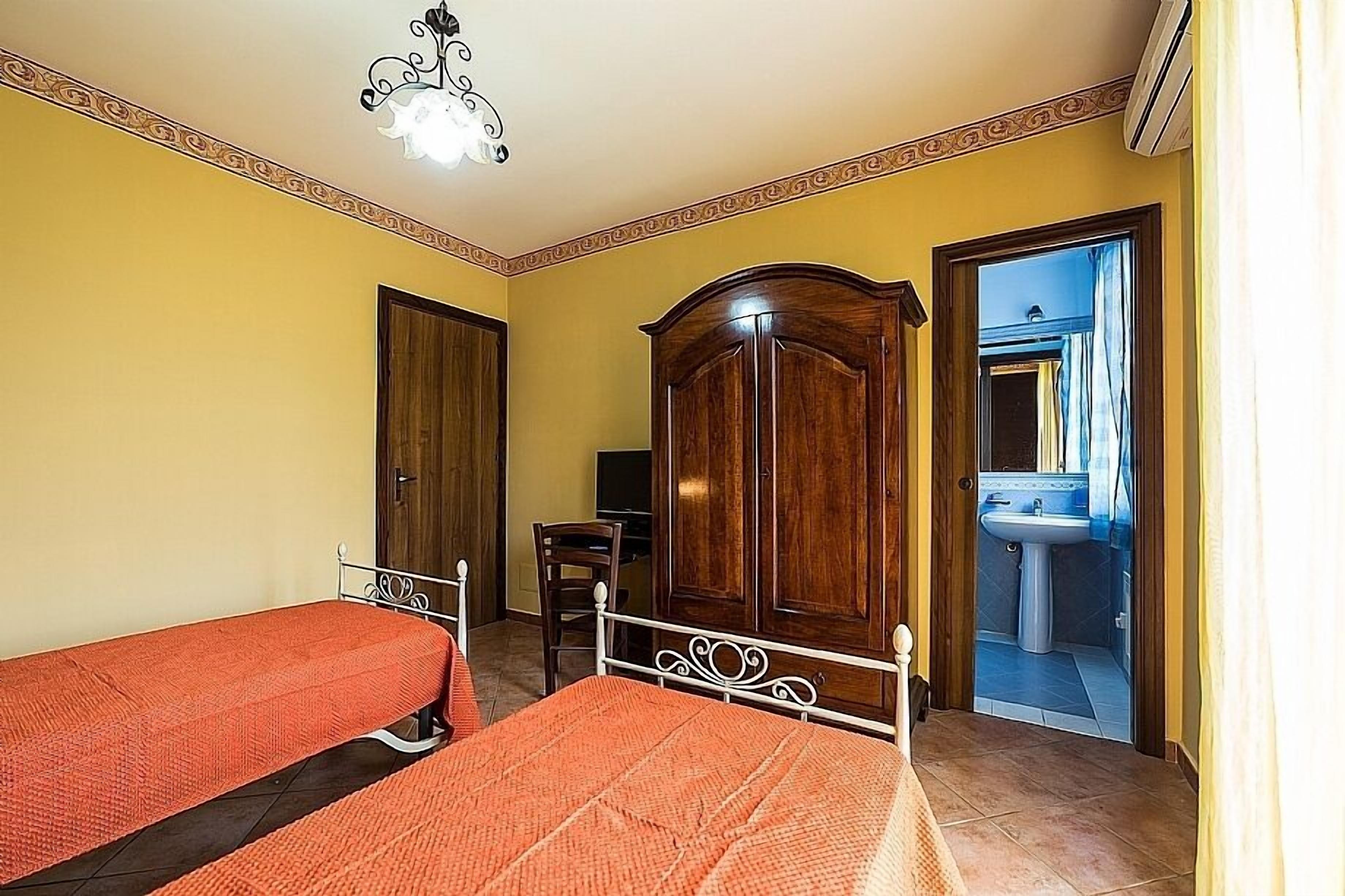 A bedroom with two single beds, a wardrobe, a desk, and a bathroom visible through an open door.