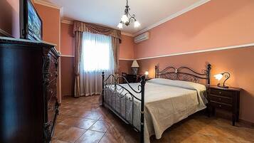 A bedroom with a bed, a dresser, a nightstand with a lamp, and a window with curtains.