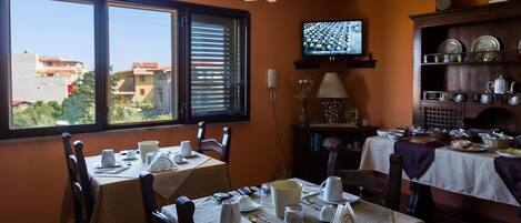 A dining area with tables set for breakfast, a television on the wall, and a view of buildings outside.