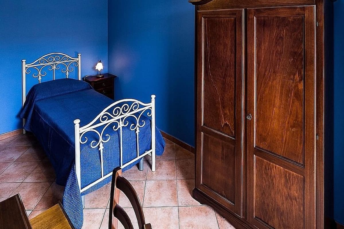 A bedroom with a bed, a wooden wardrobe, a desk with a chair, and a hanging light fixture.