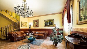 A living room with a brown leather sofa, a blue coffee table, a chandelier, a piano, and a staircase. - Bed & Breakfast Marina D'Aspra (Bagheria)