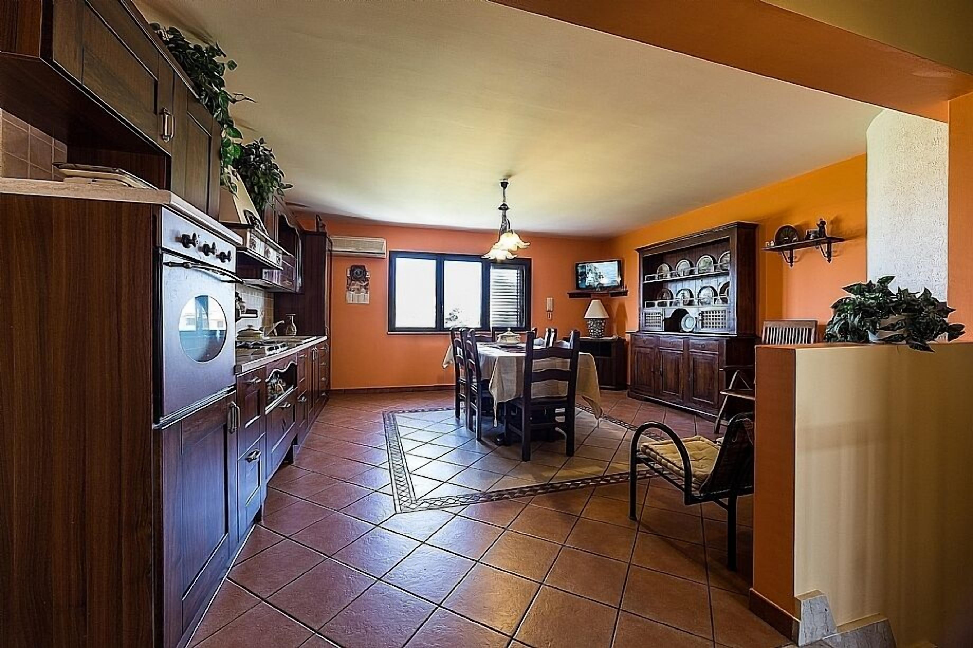 A kitchen with wooden cabinets, a dining table with chairs, and a tiled floor.