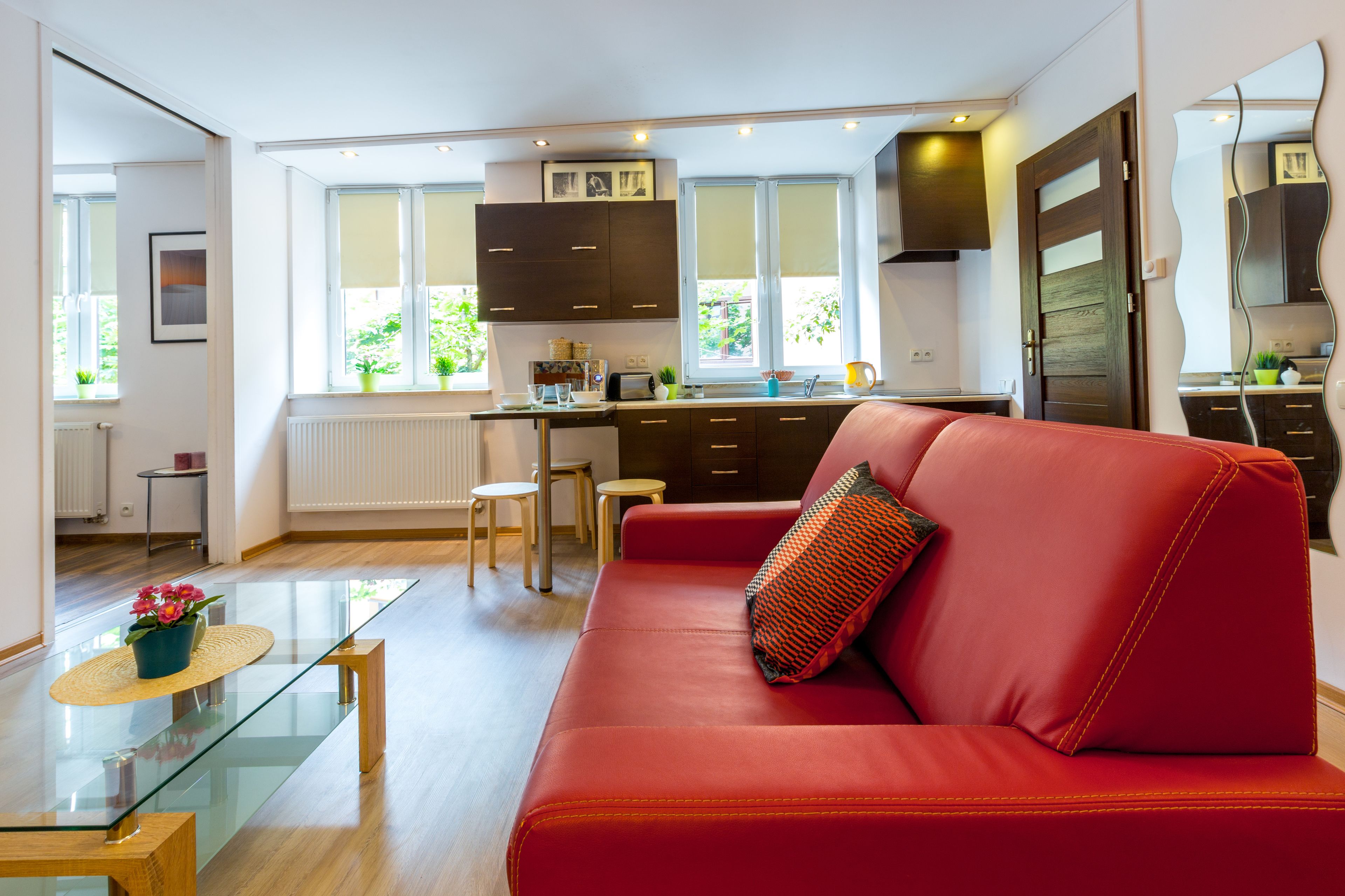 A modern kitchen with dark cabinets, a red sofa, and a glass dining table.
