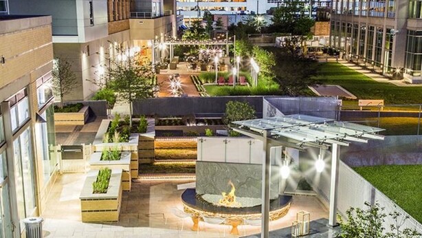 An outdoor courtyard with a central fire feature, seating areas, and a well-lit environment. - Bridgestreet the View at Liberty Center (Arlington)