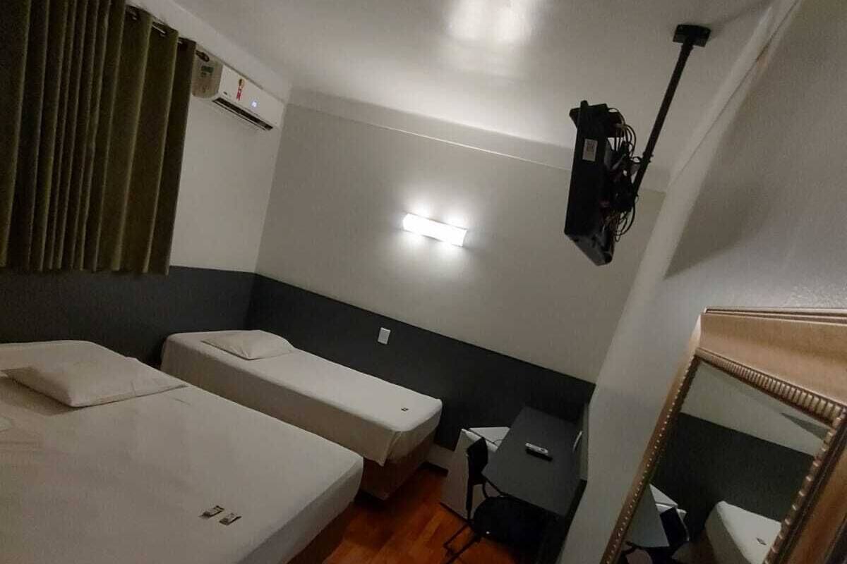 Habitación de hotel con dos camas individuales, un escritorio pequeño, un espejo y un aire acondicionado instalado en el techo.
