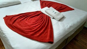 Un lit avec des draps blancs et des oreillers rouges, une serviette blanche et une couverture rouge pliée en forme de cœur.