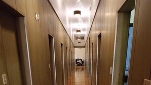 Un long couloir au sol en bois poli, avec des portes de chaque côté, menant à des pièces individuelles.